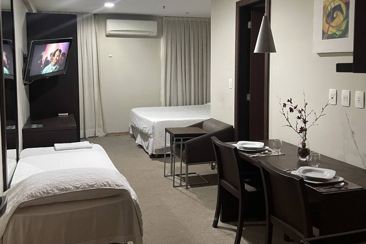 Une chambre d’hôtel avec deux lits, une table à manger avec des chaises, une télévision et un tableau au mur.