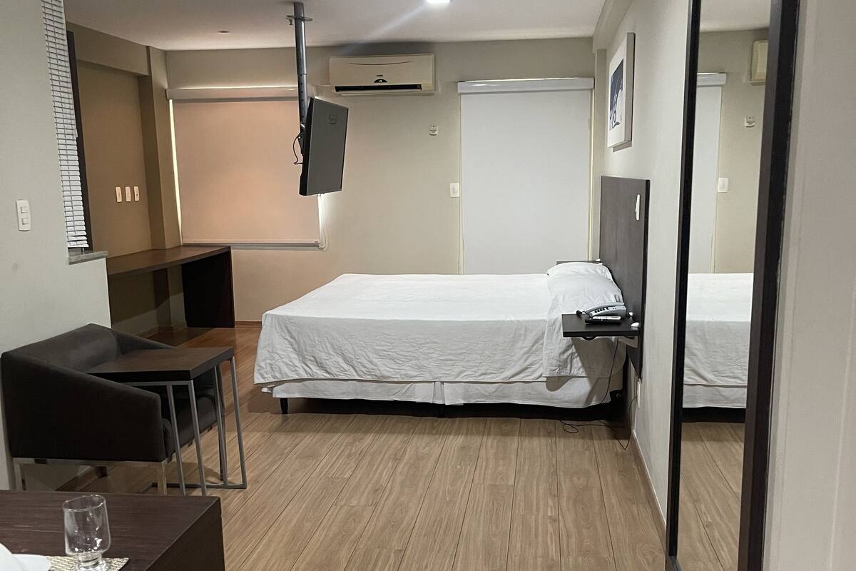 Une chambre d’hôtel avec un lit, un bureau, une chaise, une télévision et un grand miroir.