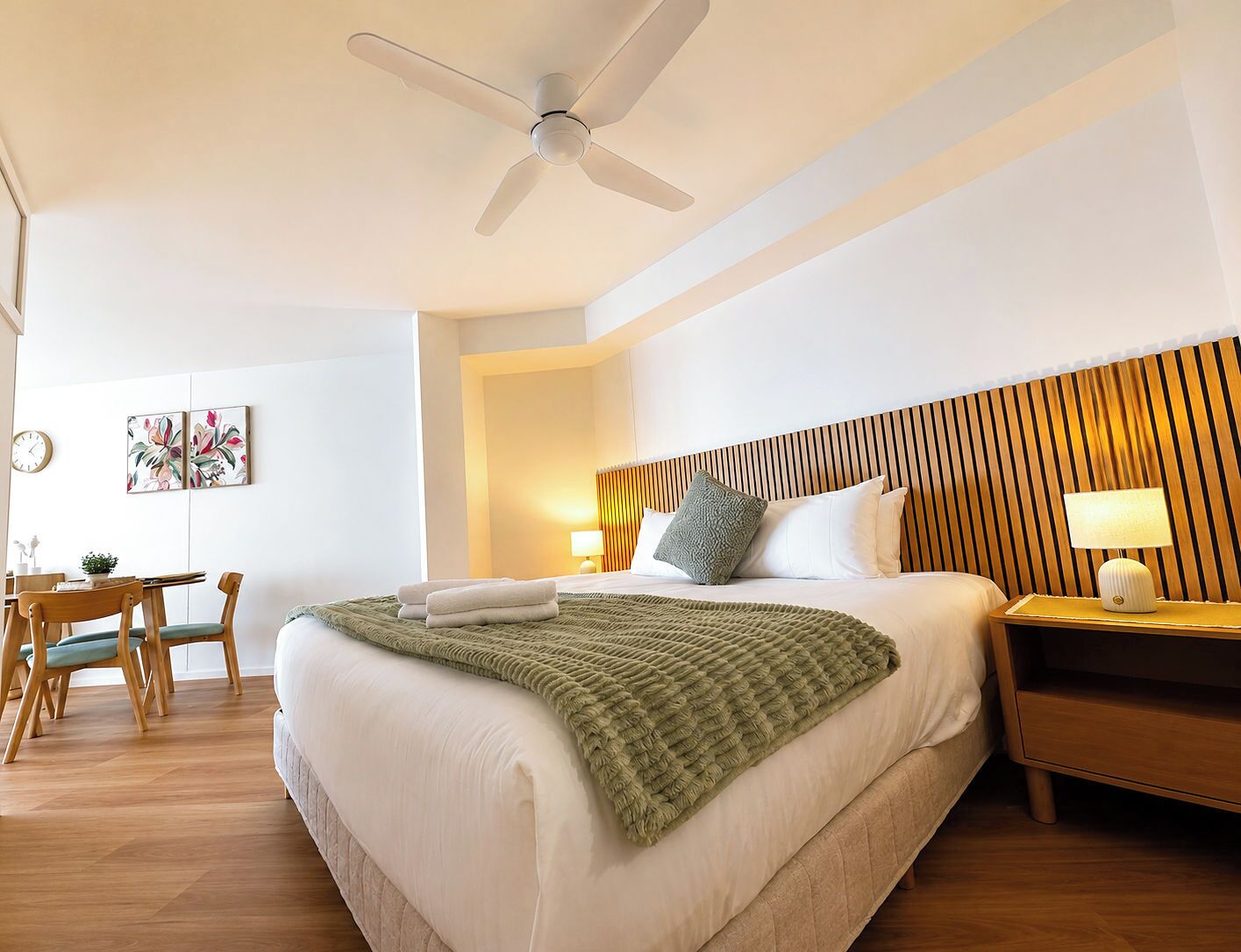 A hotel room with a bed, a desk, a chair, a lamp, and a ceiling fan.
