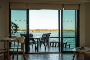 Habitación con vista al agua, una mesa con sillas y una mesita con un control remoto.