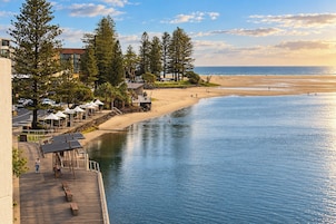 A waterfront property with a wooden deck, outdoor seating, and a view of the beach and ocean.