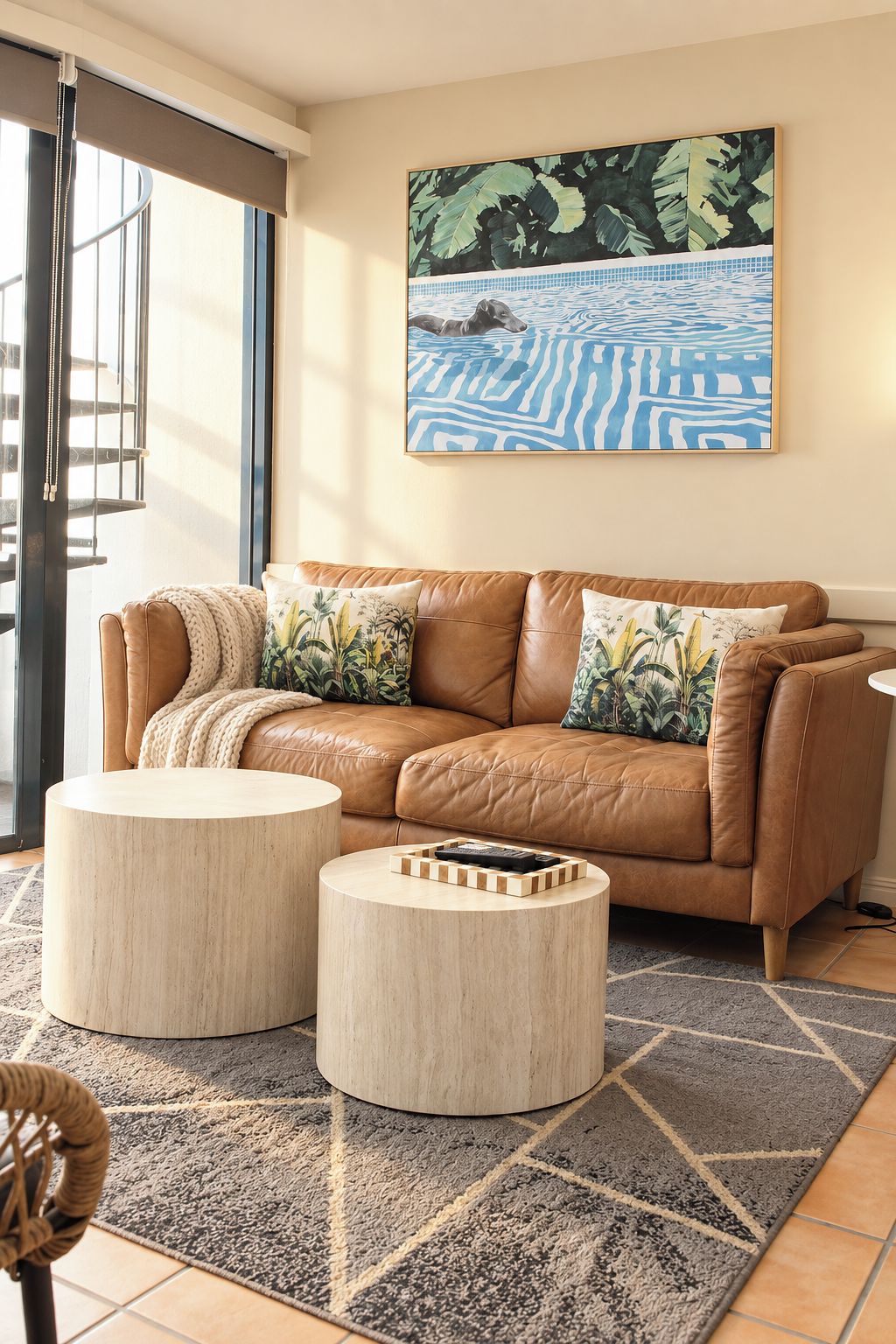 A living room with a brown leather sofa, two round wooden side tables, a patterned rug, and a large abstract painting on the wall.