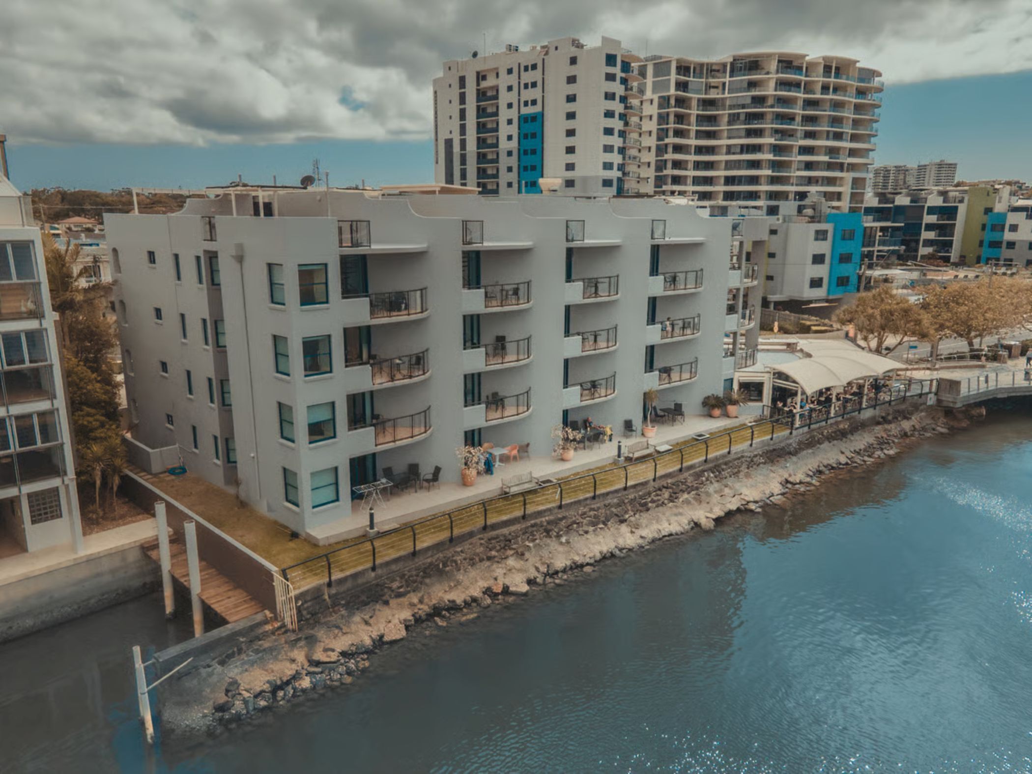 Um edifício moderno de vários andares com varandas, vista para a água e uma ponte para pedestres.