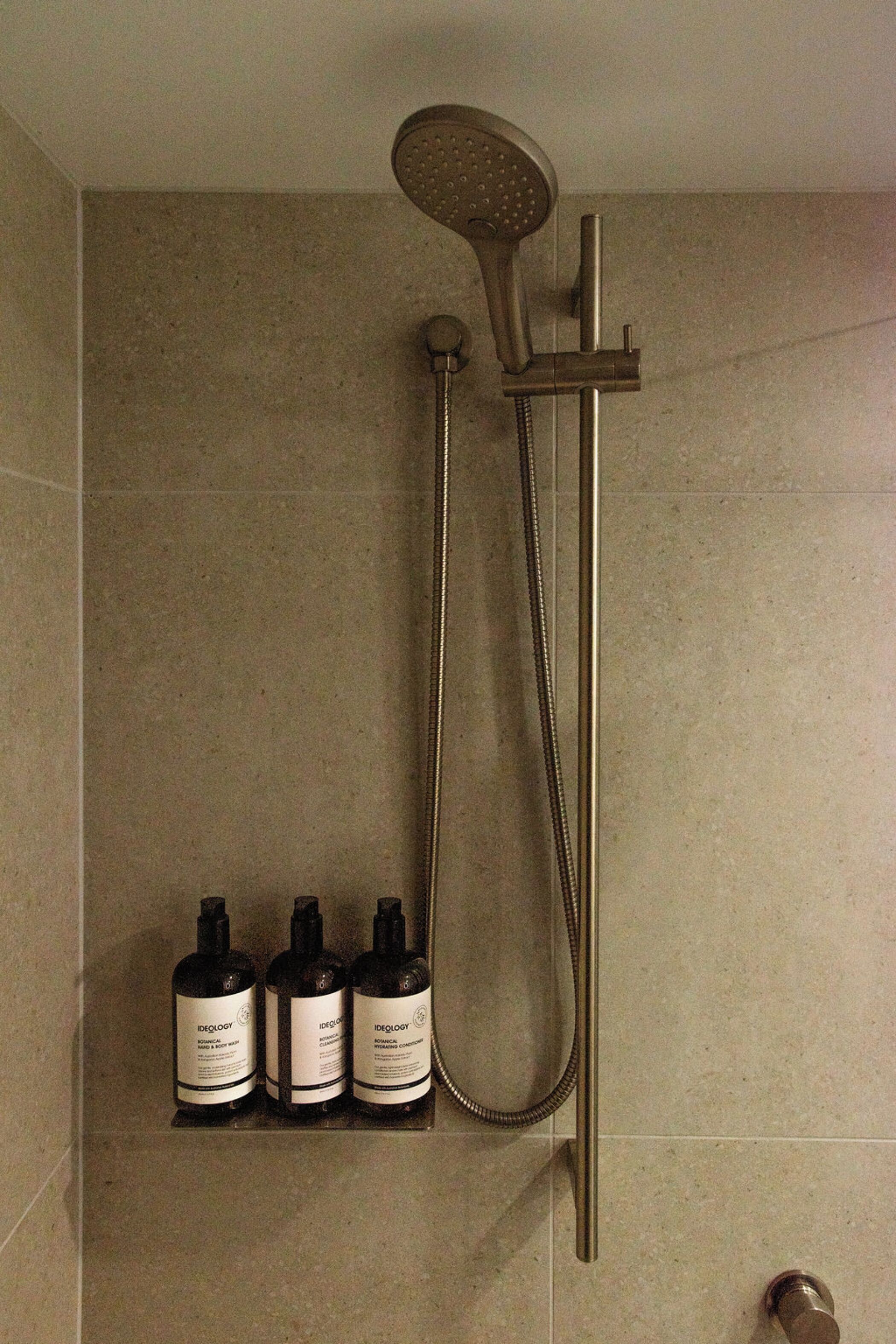 Um chuveiro com um chuveiro de mão e uma torneira fixa na parede, com três frascos de shampoo na parede.