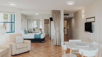 A hotel room with a bed, a sitting area with a chair and table, a TV mounted on the wall, and a large window.