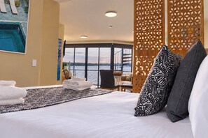 Ein Hotelzimmer mit einem großen Bett, Blick auf das Wasser und einem Balkon mit Geländer.