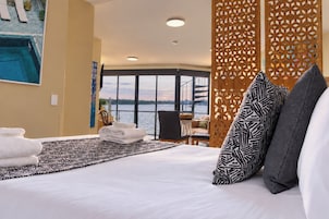 A hotel room with a large bed, a view of the water, and a balcony with a railing.