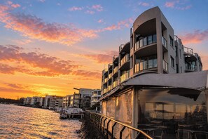 Ein Gebäude am Wasser mit mehreren Balkonen, einer Glasfassade und Blick auf das Wasser.