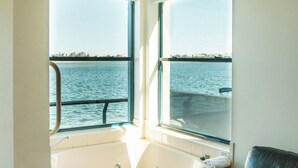 A corner room with a bathtub, a window with a view of the water, and a dark-colored sofa with a pillow. - La Promenade Absolute Waterfront Apartments (Caloundra)