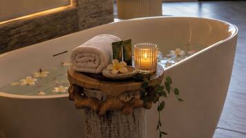 A spa tub with a towel and candles, a wooden stool, and a view of the sea.