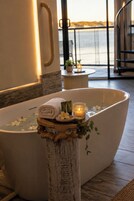 A spa tub with a towel and candles, a wooden stool, and a view of the sea.