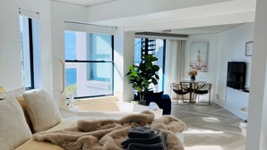 A spacious bedroom with a large bed, a view of the outdoors, a dining area, and a TV. - La Promenade Absolute Waterfront Apartments (Caloundra)