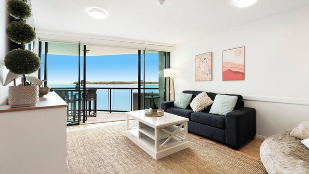 A living room with a sofa, coffee table, and artwork on the wall. - La Promenade Absolute Waterfront Apartments (Caloundra)
