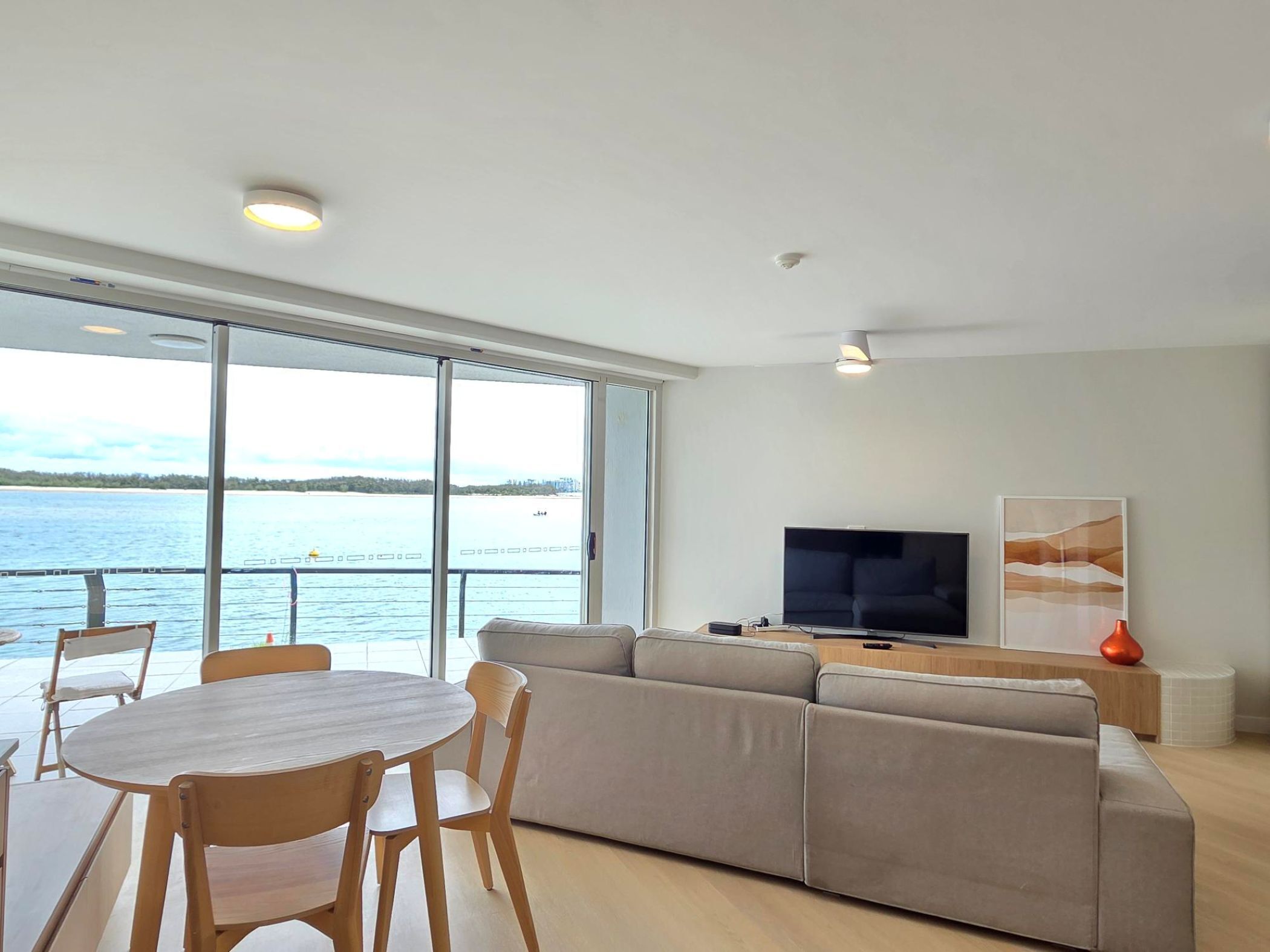 Uma sala de estar moderna com uma grande janela, um sofá, uma televisão e uma área de jantar com mesa e cadeiras.