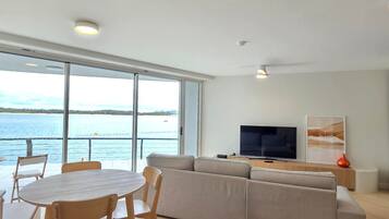 Uma sala de estar moderna com uma grande janela, um sofá, uma televisão e uma área de jantar com mesa e cadeiras.