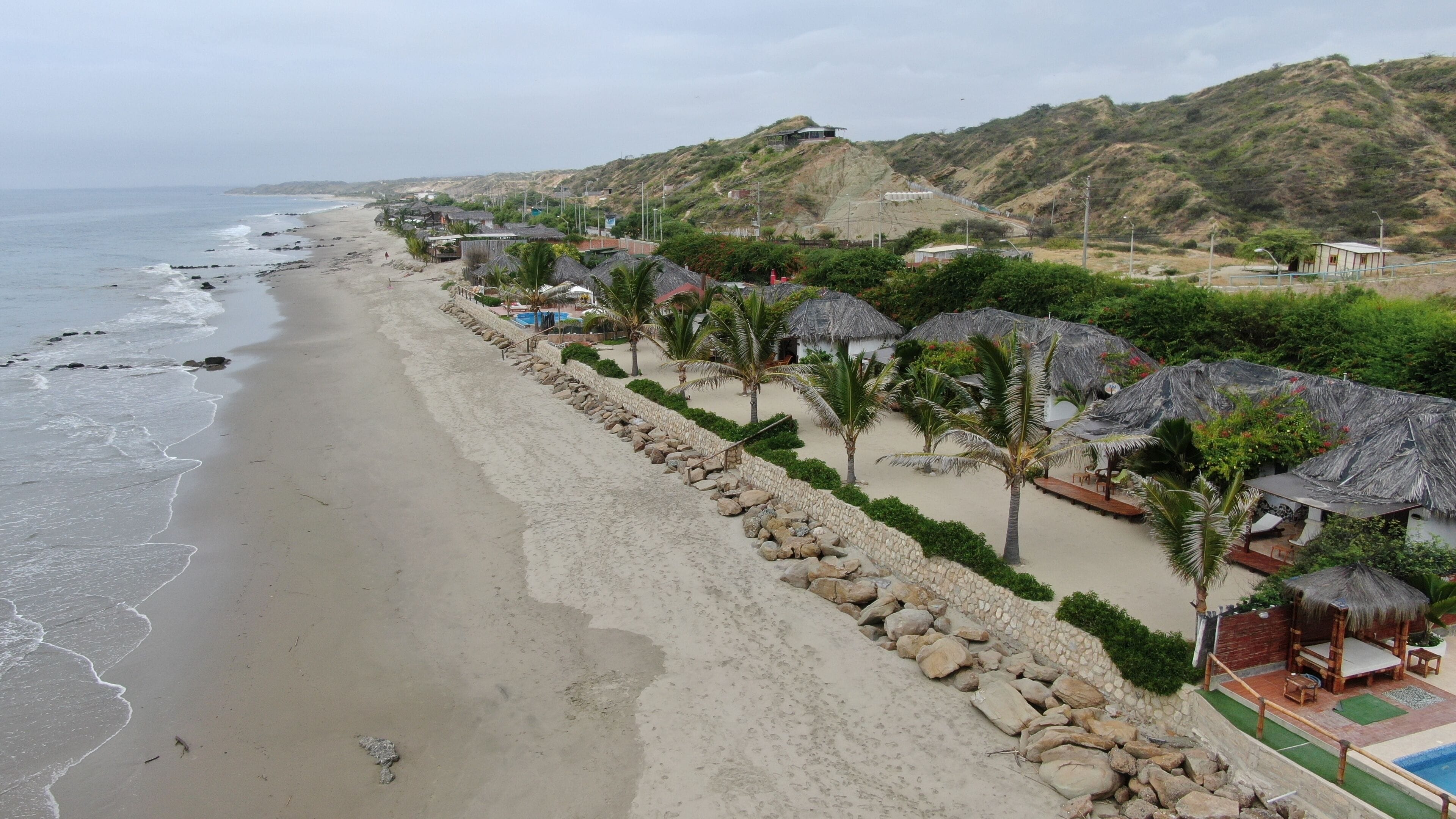 Un resort en la playa con cabañas de techo de paja, una playa arenosa y vista al océano.