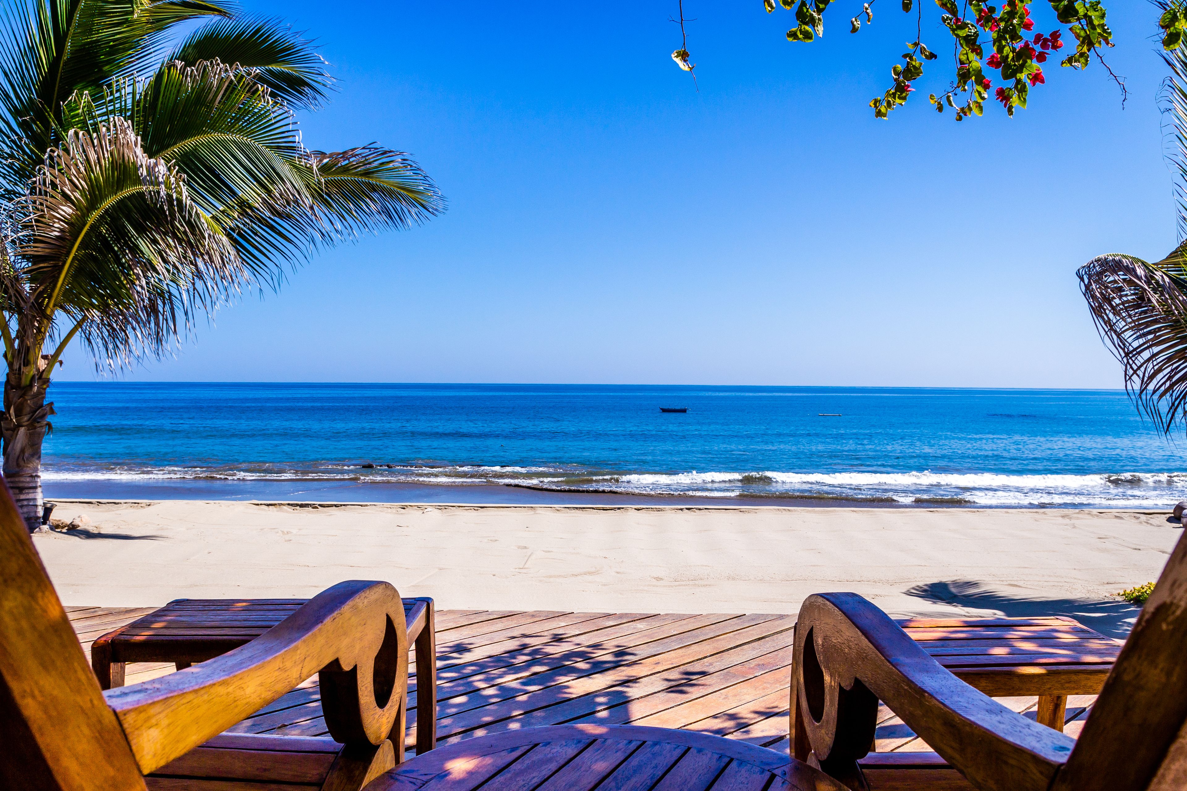 Une terrasse en bois avec des chaises donnant sur une plage et l’océan.