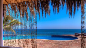 Blick auf einen Pool, einen strahlend blauen Himmel, eine Steinterrasse und den Ozean.