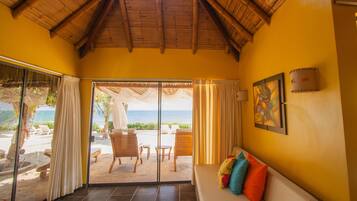 A room with a view of the beach, a sofa with colorful cushions, and a painting on the wall.