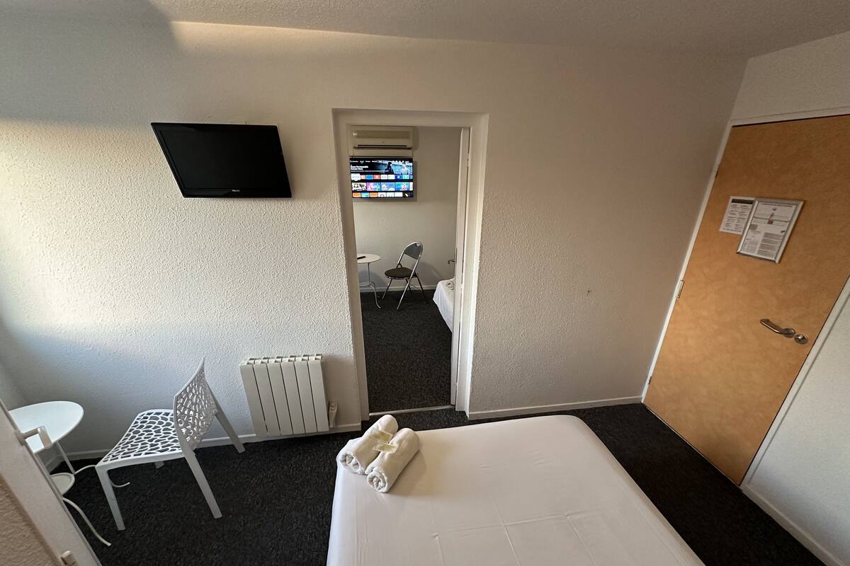 A hotel room with a bed, a TV mounted on the wall, a small table, and a chair.