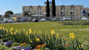 A hotel with a modern design, featuring a central courtyard with a variety of flowers and a fenced parking area. - Hôtel L'ESCALE d'Alès (Ales)