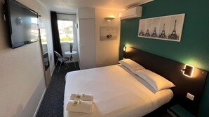 A hotel room with a bed, a TV, a small table with a chair, and a window. - Hôtel L'ESCALE d'Alès (Ales)