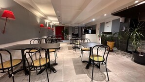 A modern dining area with multiple tables and chairs, recessed ceiling lighting, and potted plants. - Hôtel L'ESCALE d'Alès (Ales)