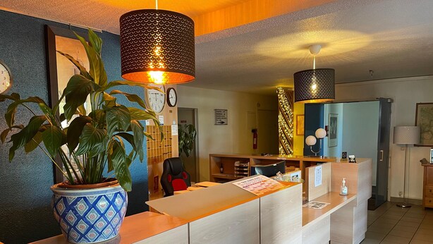 A reception desk with a potted plant, a clock, and a framed picture on the wall. - Hôtel L'ESCALE d'Alès (Ales)