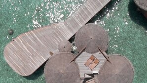 An aerial view of a resort with a central circular structure surrounded by lounge areas and a large wooden deck extending over the water. - Nika Island Resort & Spa (Kudafolhudhoo)