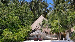 A beachfront property with a thatched-roof hut, surrounded by lush greenery and palm trees. - Nika Island Resort & Spa (Kudafolhudhoo)