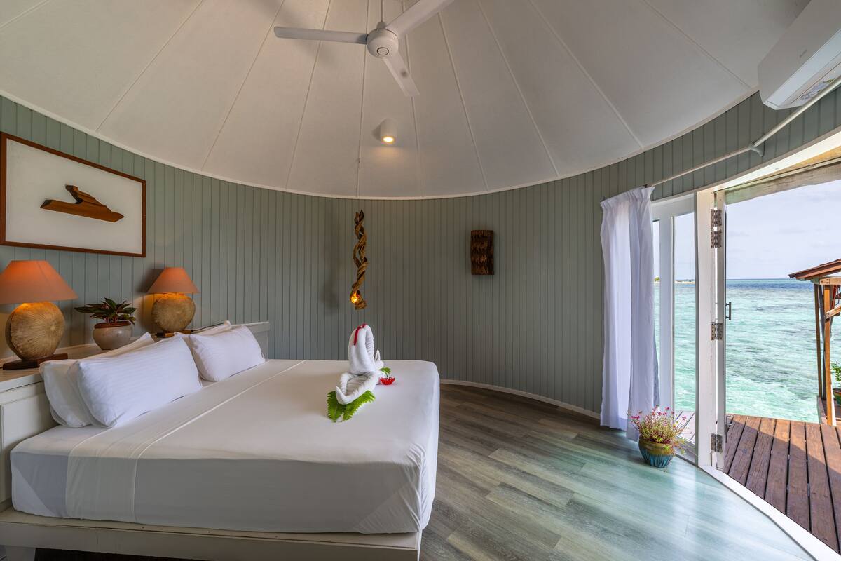 Une chambre spacieuse avec un grand lit, un ventilateur de plafond et une vue sur l’océan, accessible par une porte coulissante.