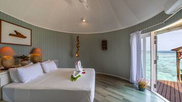 A spacious bedroom with a large bed, a ceiling fan, and a view of the ocean through a sliding door.