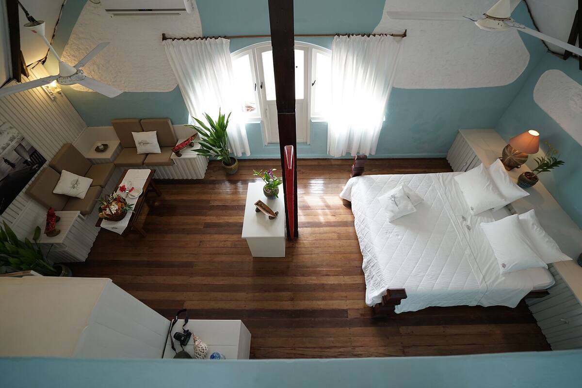 Une chambre avec un grand lit, un coin salon avec un canapé et une table, et un ventilateur de plafond.