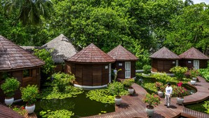 A resort with wooden huts, a pond with lily pads, and potted plants. - Nika Island Resort & Spa (Kudafolhudhoo)
