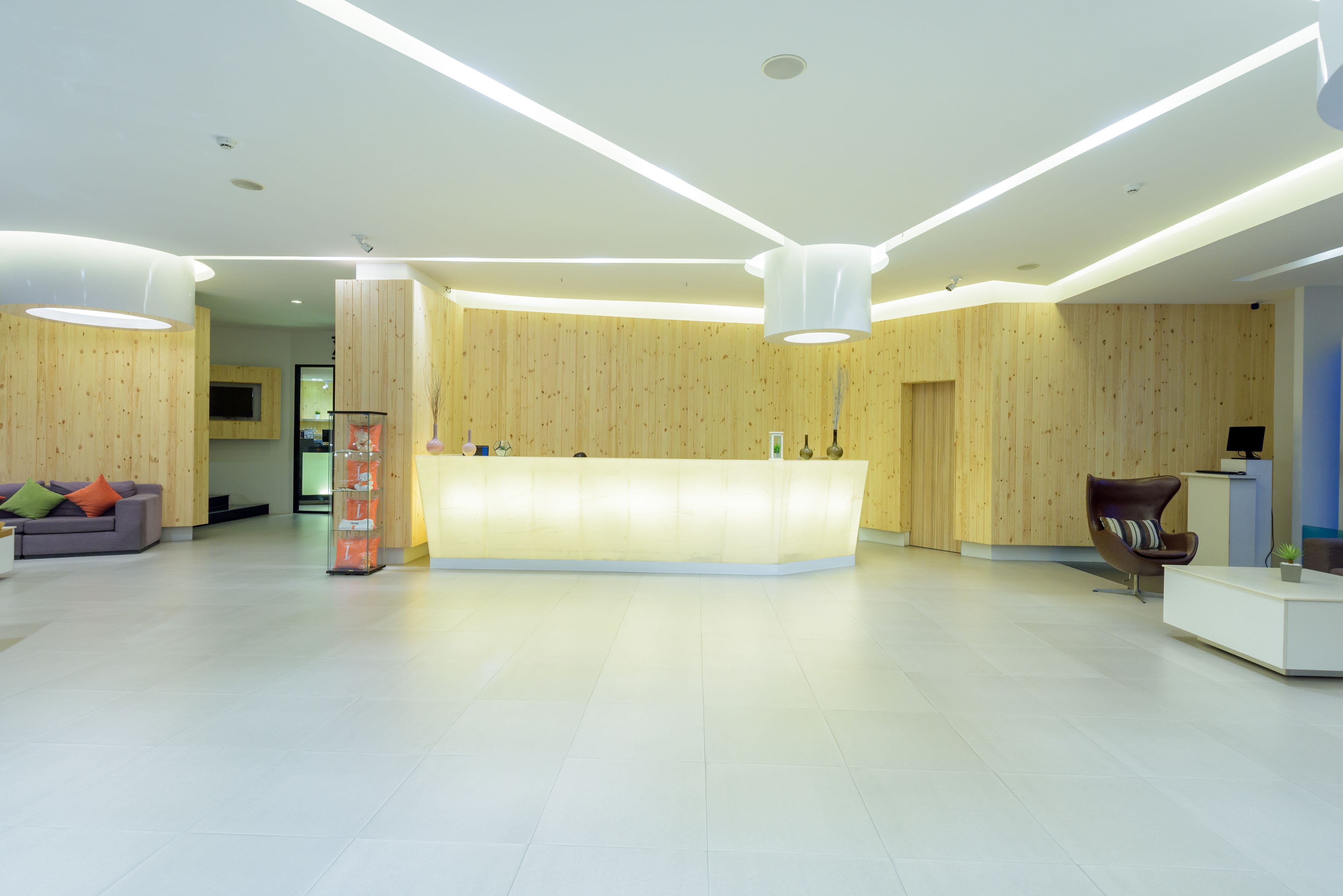 A modern reception area with a wooden reception desk, a sofa with colorful cushions, and a minimalist design.