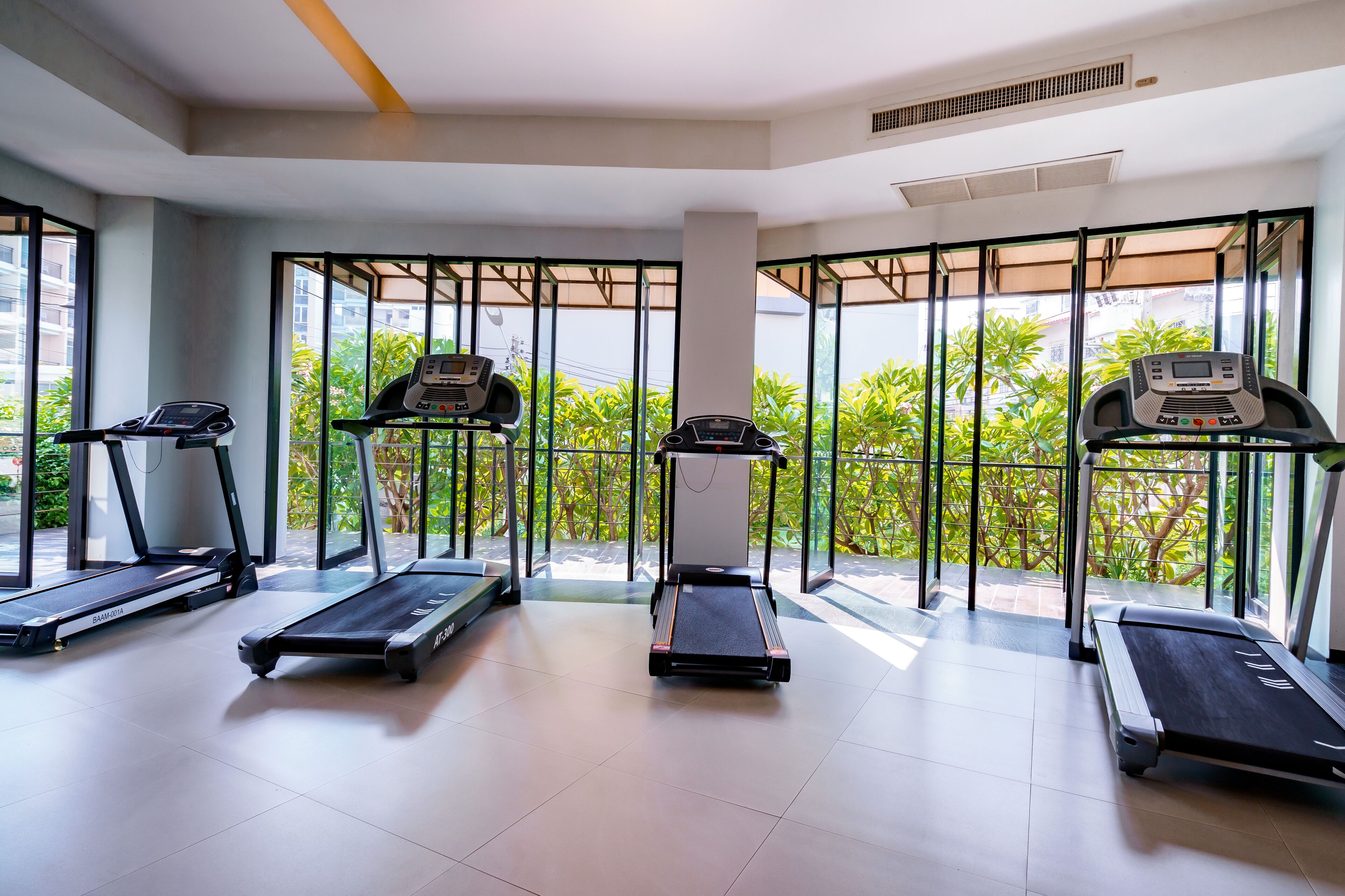 A modern gym with three treadmills, large windows, and a view of greenery.