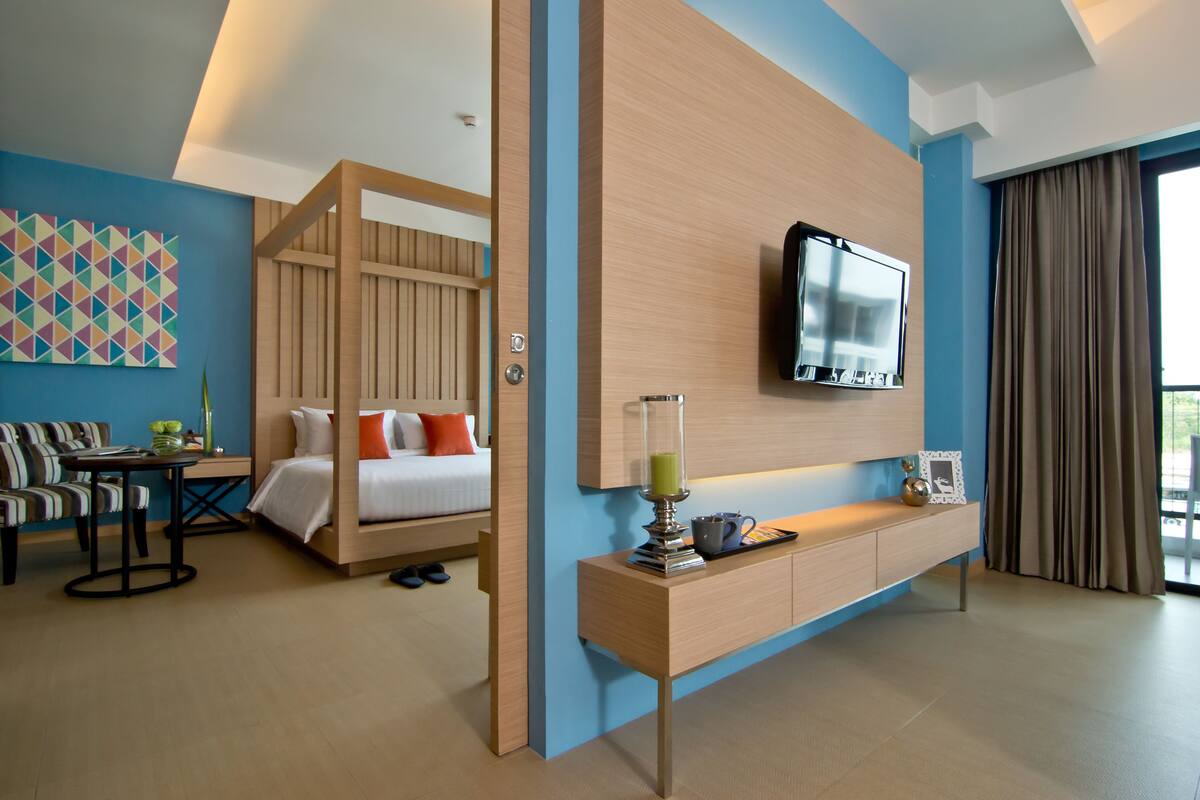 A modern hotel room with a bed, a TV, a desk, and a large window.