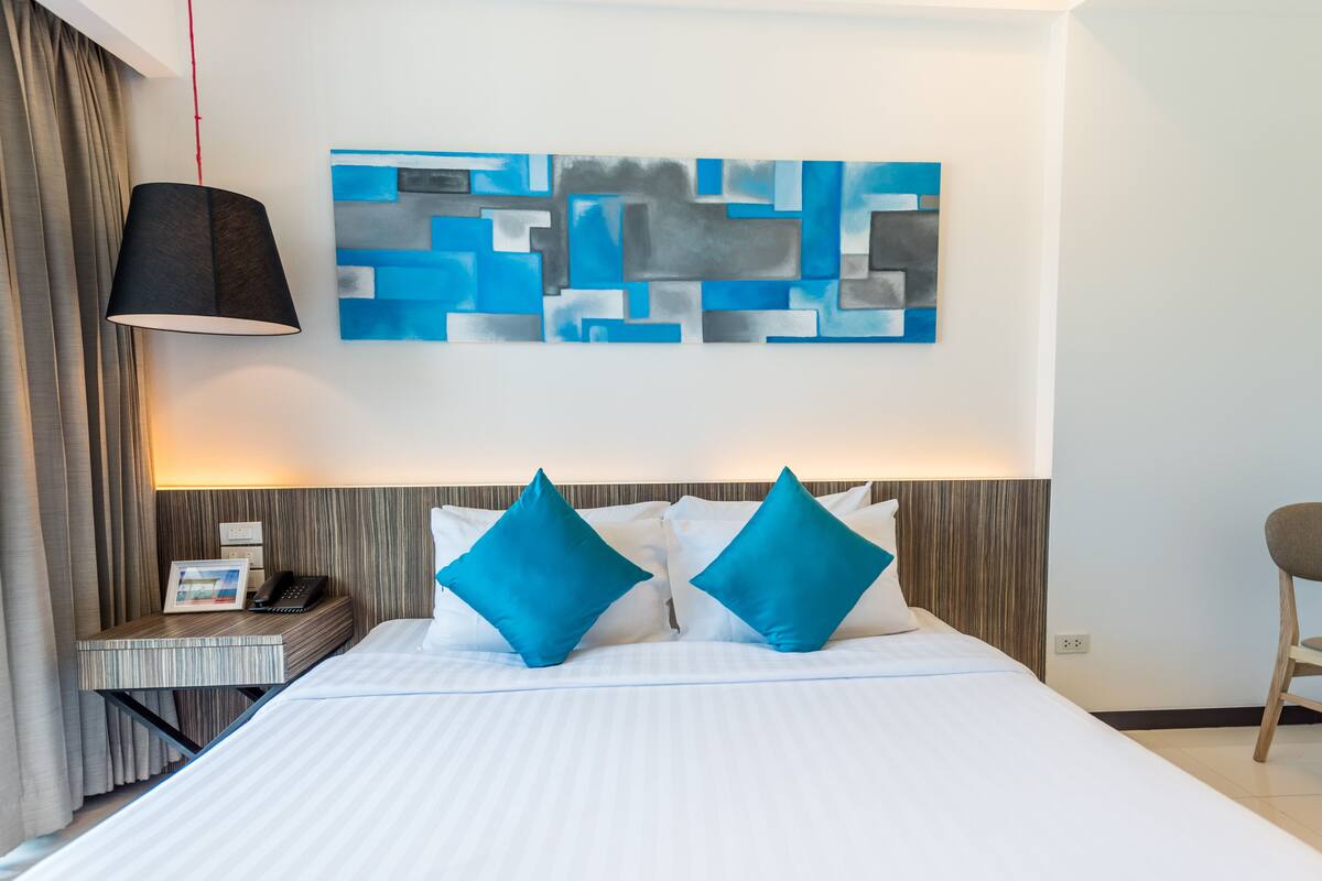 A hotel room with a bed, a nightstand with a phone, a lamp, and a wall art piece.