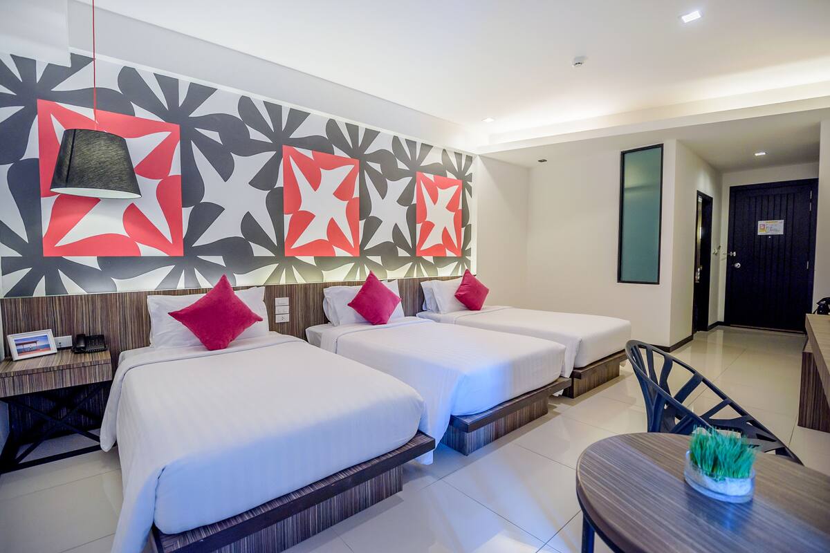 A hotel room with two beds, a desk with a phone, and a dining area with a table and chairs.