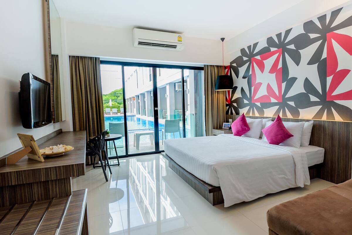 A hotel room with a bed, a TV, a desk with a chair, a small table, and a view of the outside.