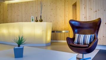 A reception area with a wooden wall, a reception desk, a modern chair with a striped pillow, and a small potted plant.