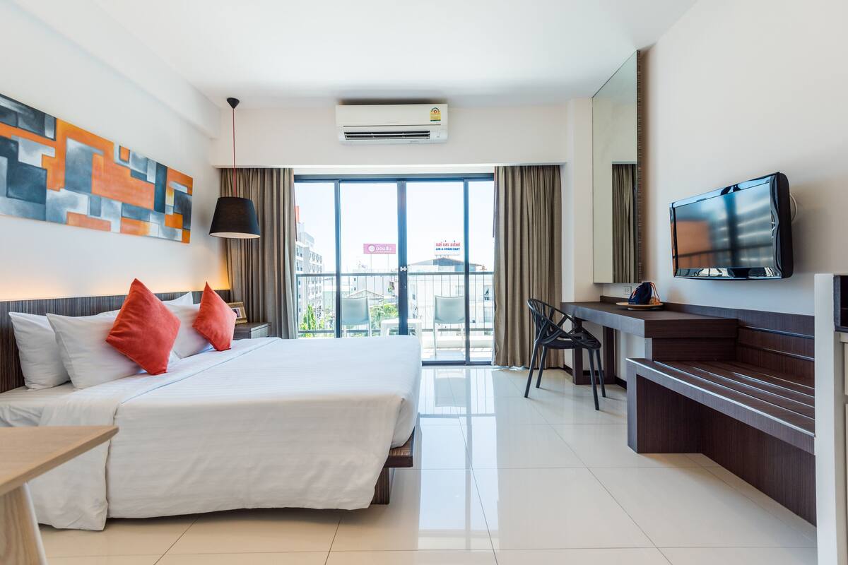 A hotel room with a bed, a desk, a TV, and a large window.