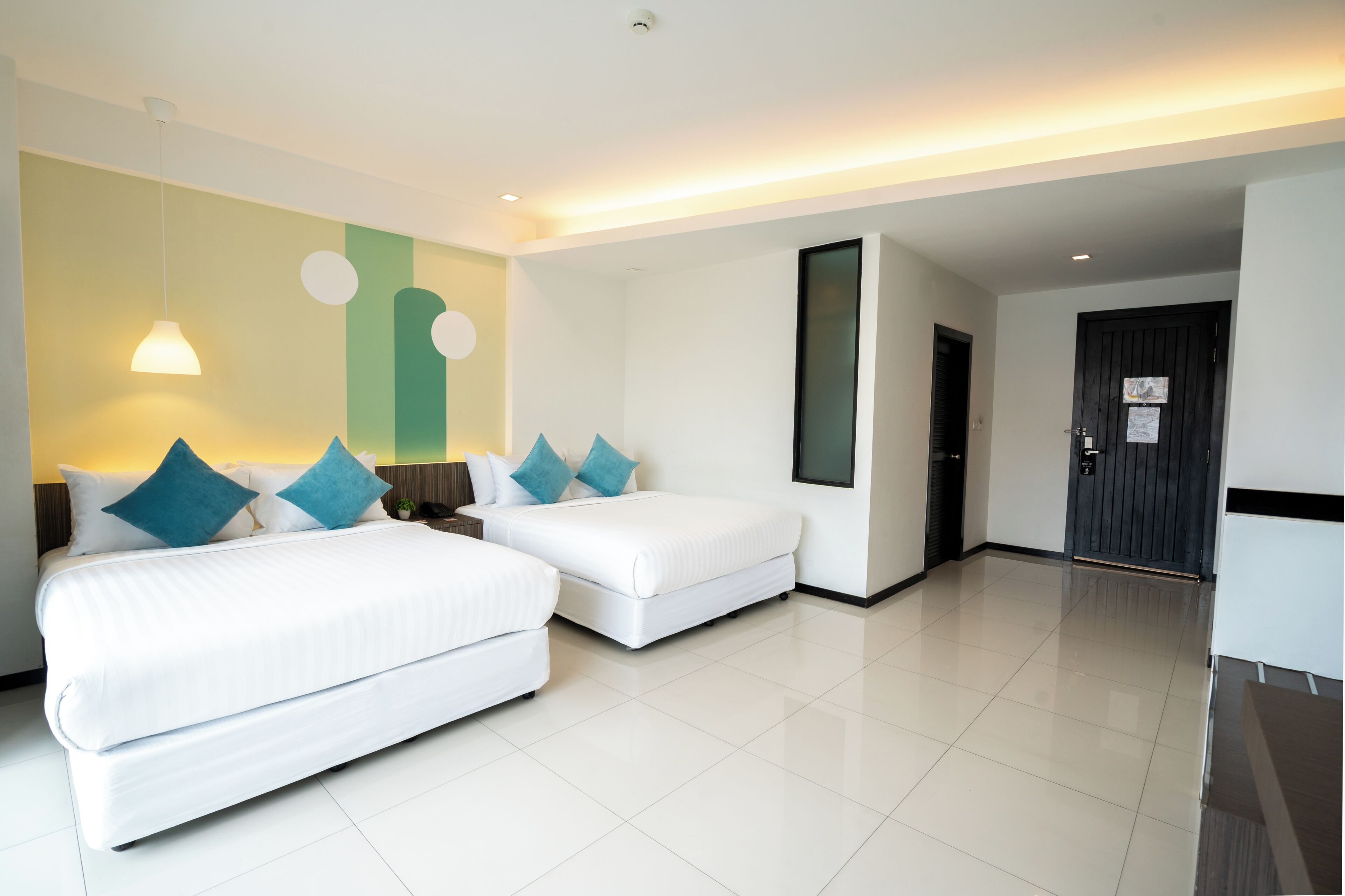 A hotel room with two beds, a desk, a chair, a small table, and a door.