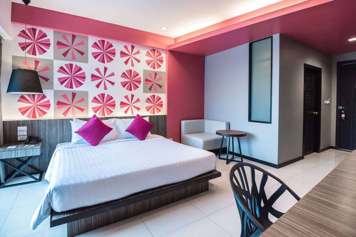 A modern hotel room with a large bed, a seating area, and a decorative wall.