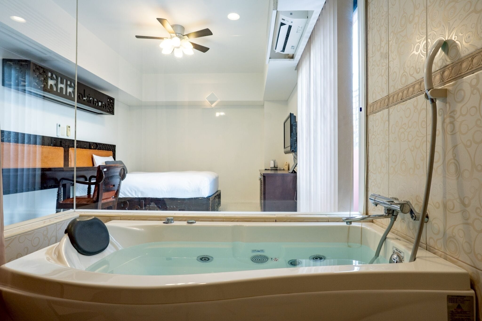 Una habitación de hotel con una bañera grande, un ventilador de techo, una cama y un televisor.