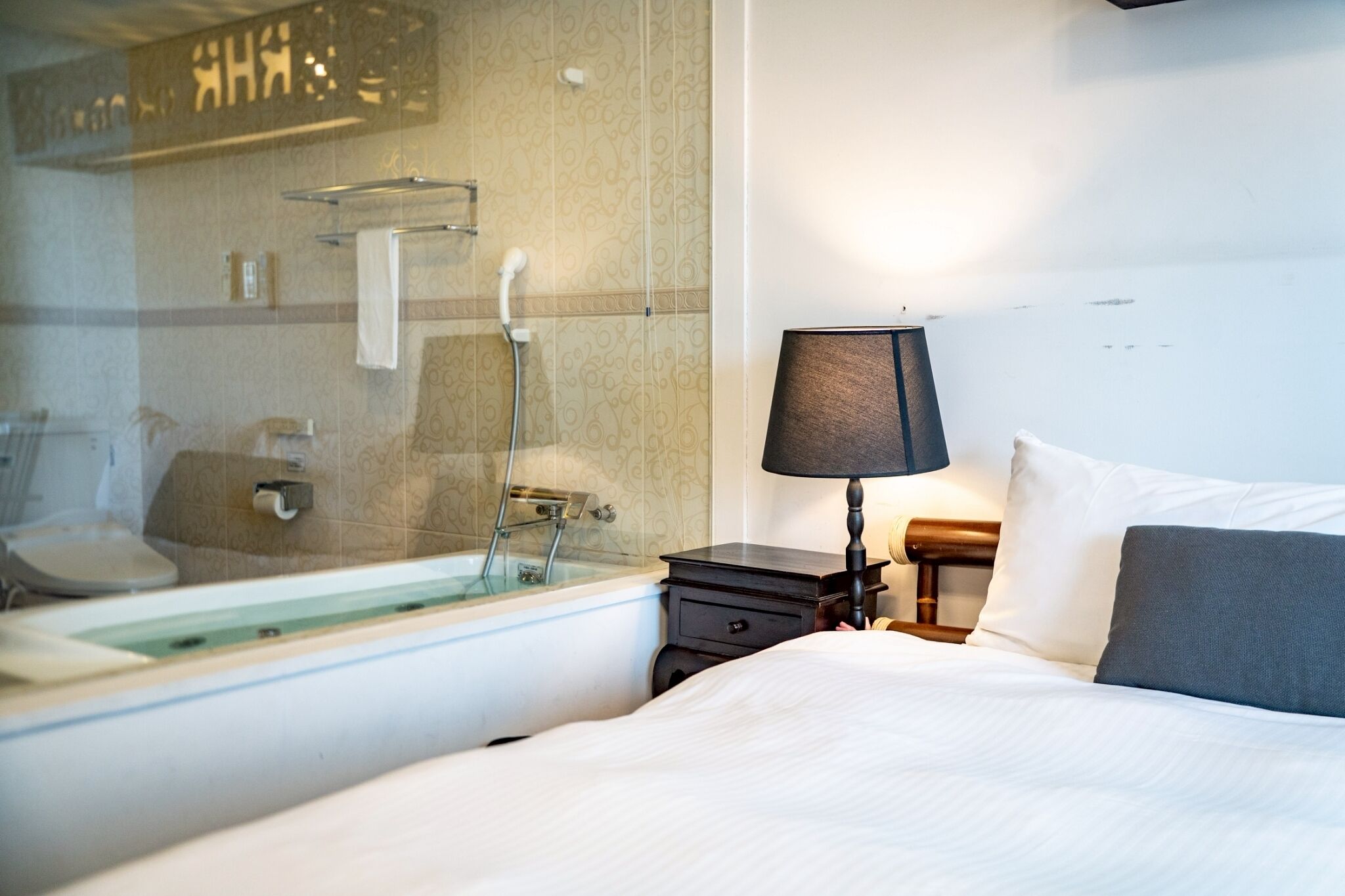 Quarto de hotel com uma cama, mesa de cabeceira com abajur, banheiro com banheira e vaso sanitário.