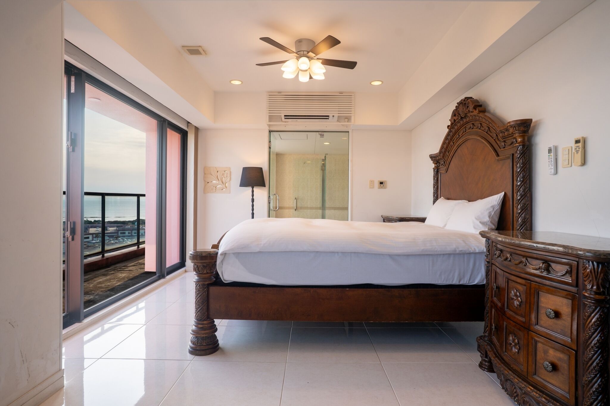 A bedroom with a large bed, a ceiling fan, a nightstand, a dresser, and a sliding glass door leading to a balcony.