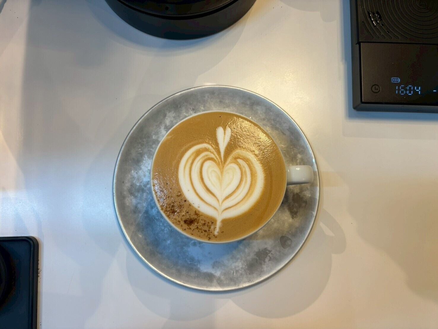 Una taza de café con un dibujo artístico en espuma sobre un plato metálico.