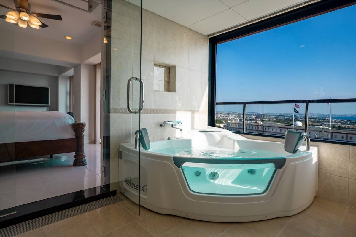 A modern hotel room with a large bathtub, a bed, a television, and a city view.