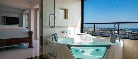A modern hotel room with a large bathtub, a bed, a television, and a city view.